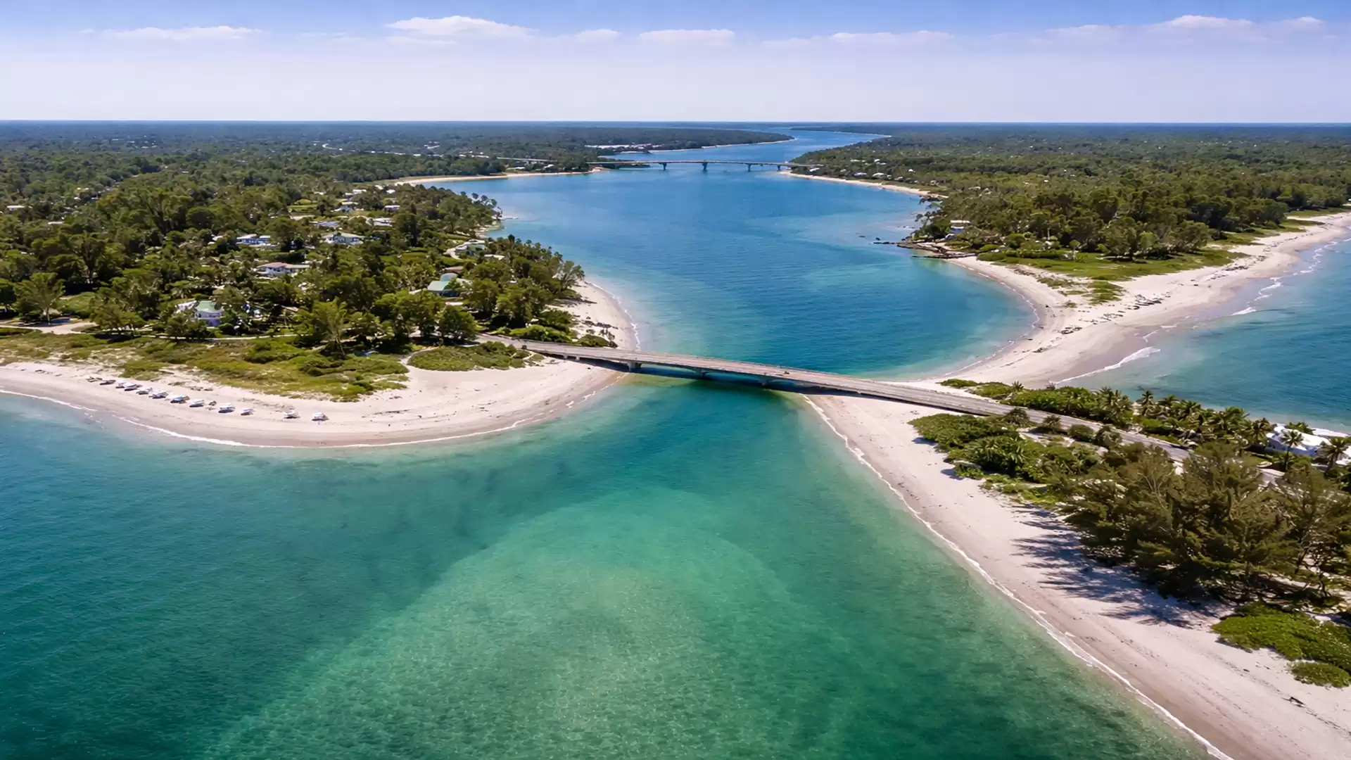 Aerial view of a picturesque coastal landscape with clear turquoise water, sandy beaches, and a bridge connecting two shores.