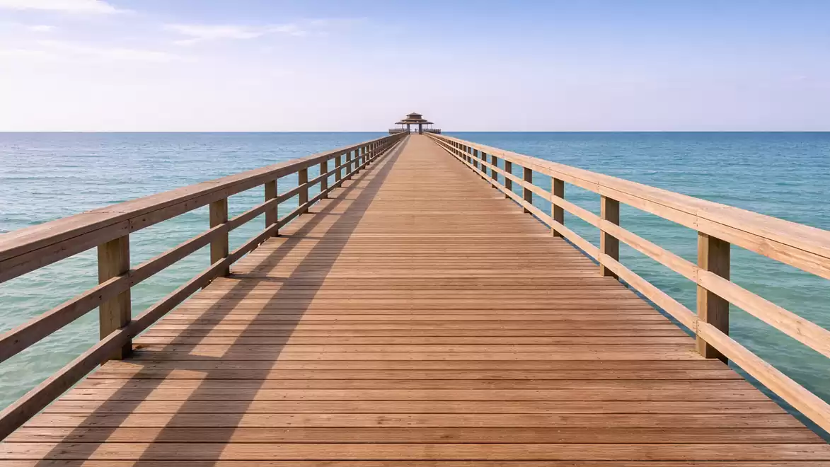 A long wooden pier extends into the sea with a clear blue sky in the background.