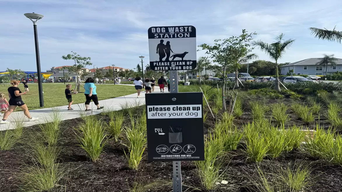 A dog waste disposal area in a park with grass and walkers in the background.