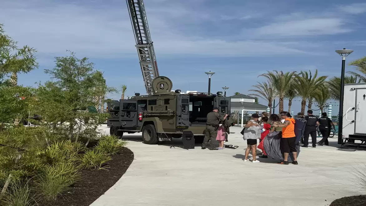 A group of people stands next to an emergency vehicle with an extended ladder in a park with palm trees and a modern setting.
