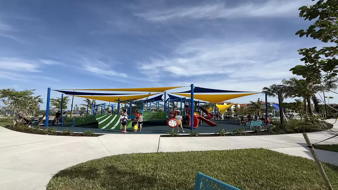 Children playing on a playground at Jaycee Park in Cape Coral, Florida, surrounded by green areas and shade sails under a blue sky.