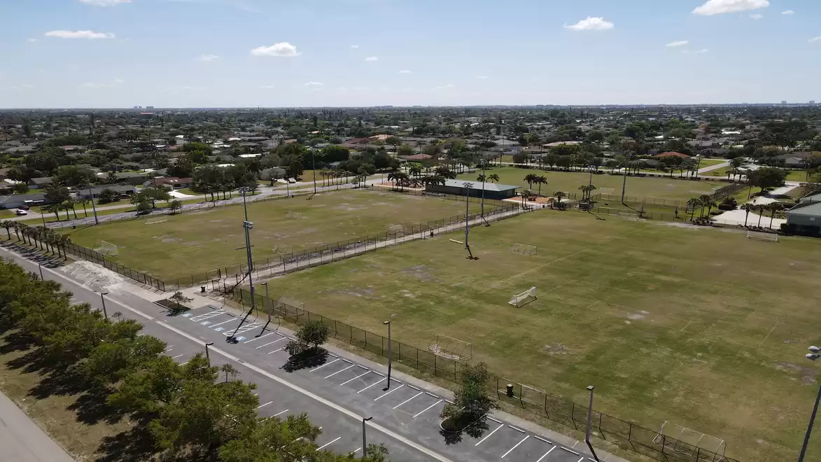 Aerial view of an empty sports field in a suburban area with multiple soccer pitches and a quiet parking lot.
