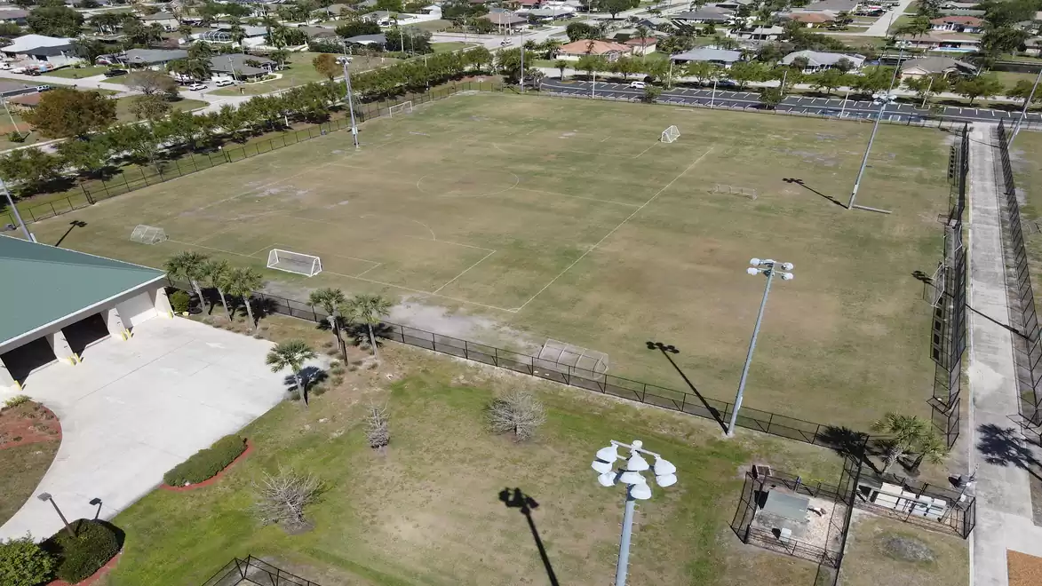 Aerial view of a large, fenced soccer field with goals, surrounded by residential houses.