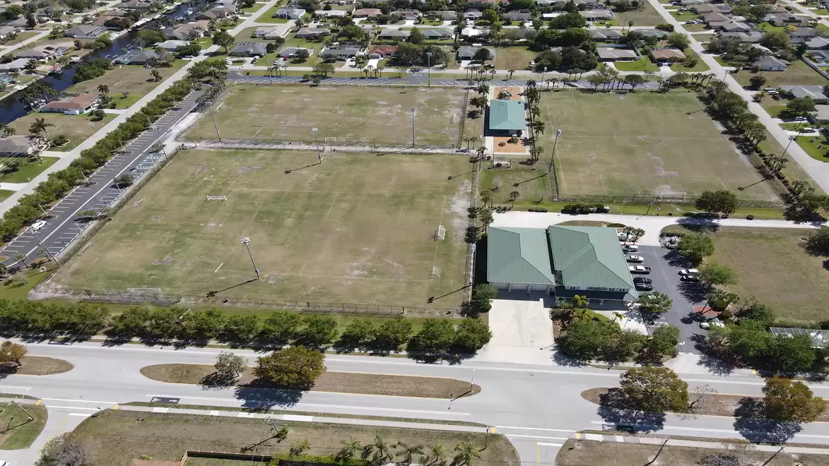 Aerial view of a sports complex with several open playing fields and an adjacent residential area.