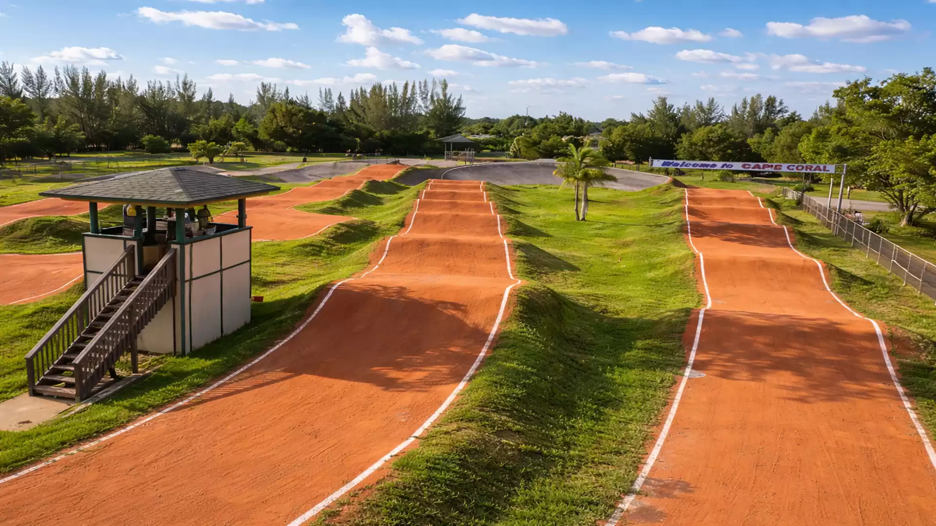 A BMX racetrack with red dirt tracks under a blue sky, surrounded by green vegetation.