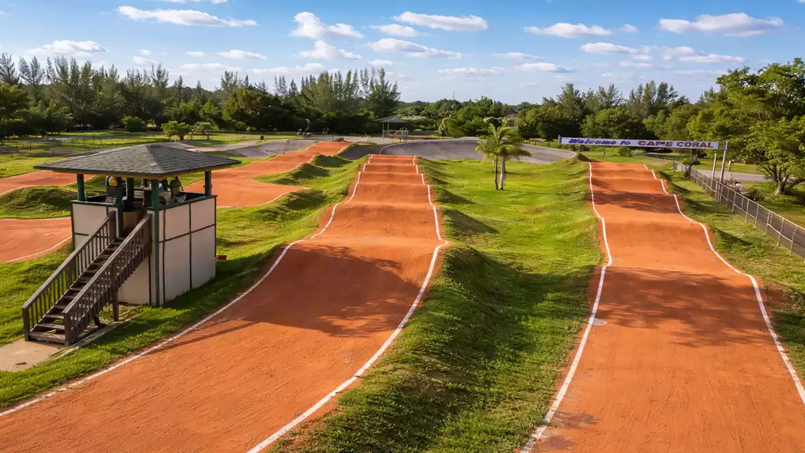 A BMX racetrack with red dirt tracks under a blue sky, surrounded by green vegetation.