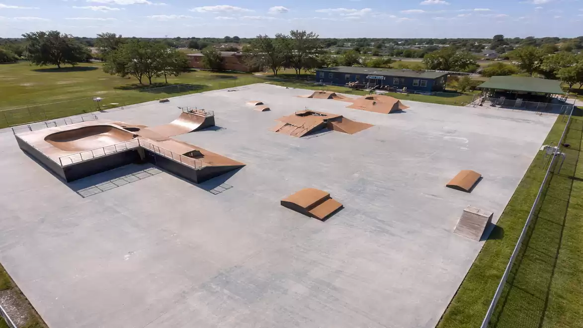 A modern skatepark with various ramps and obstacles, surrounded by green areas under a clear blue sky.