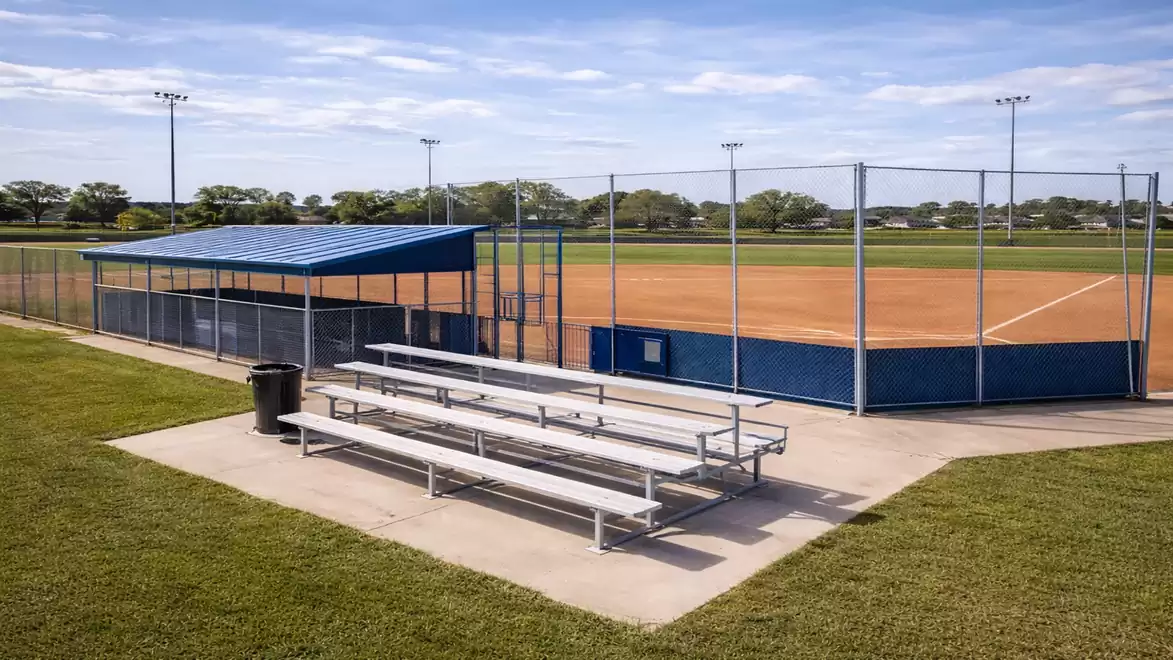 Empty baseball field with bleachers and blue fencing on a sunny day.