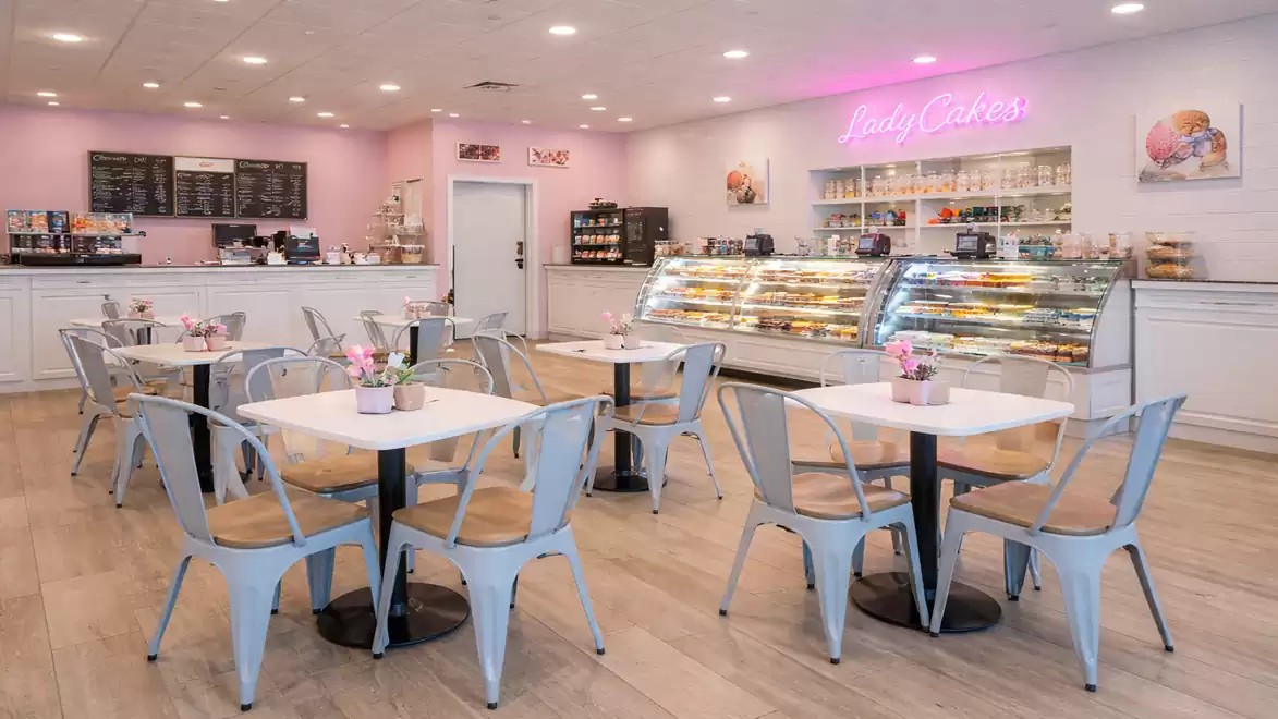 Interior view of a cozy café with pink walls, white furniture, and a cake display area.