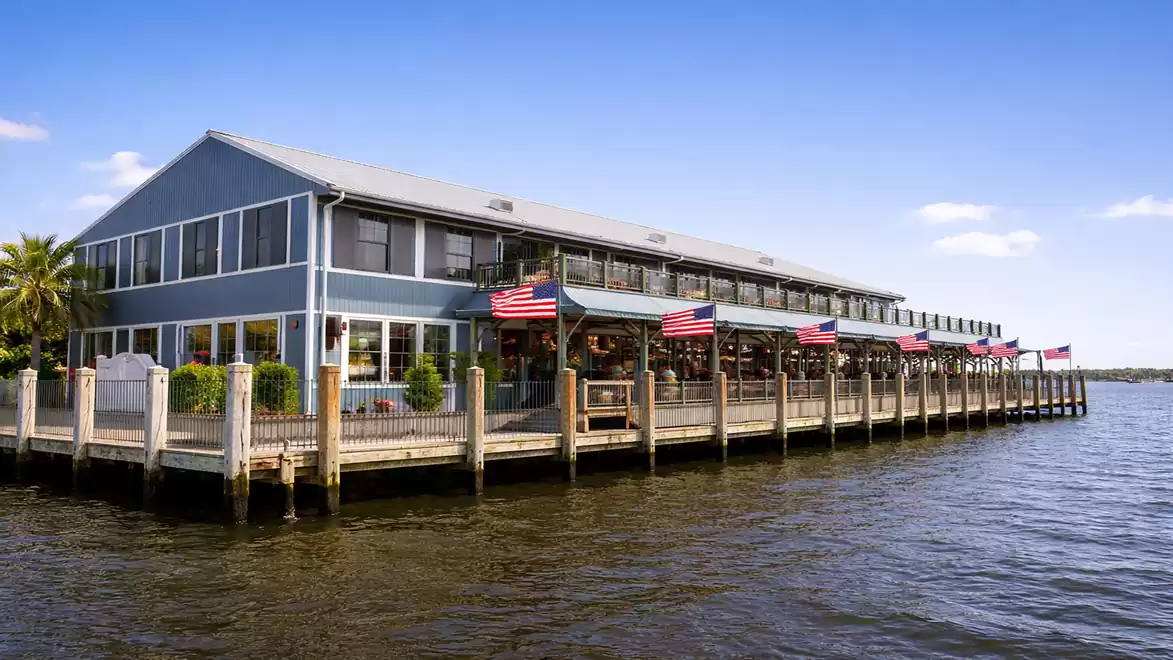 A large building by the water with American flags and a blue facade under a clear sky.