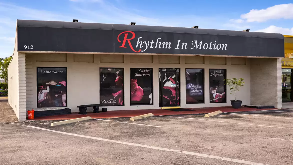 Exterior view of a dance studio with large windows and the sign 'Rhythm In Motion'.