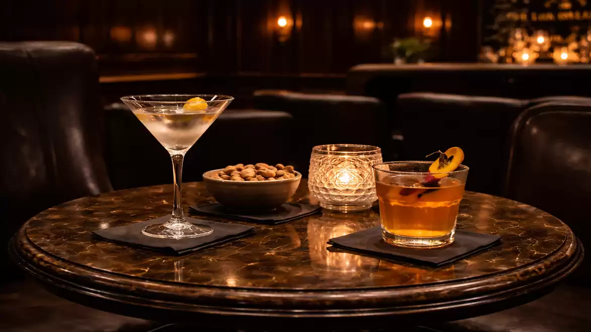 Elegant bar atmosphere with a table featuring a Martini, an Old Fashioned cocktail, nuts, and candlelight.