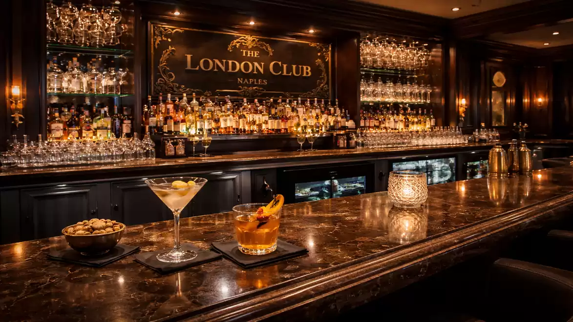 Elegant bar at The London Club with fine cocktails on a marble countertop, surrounded by a luxurious ambiance and dim lighting.