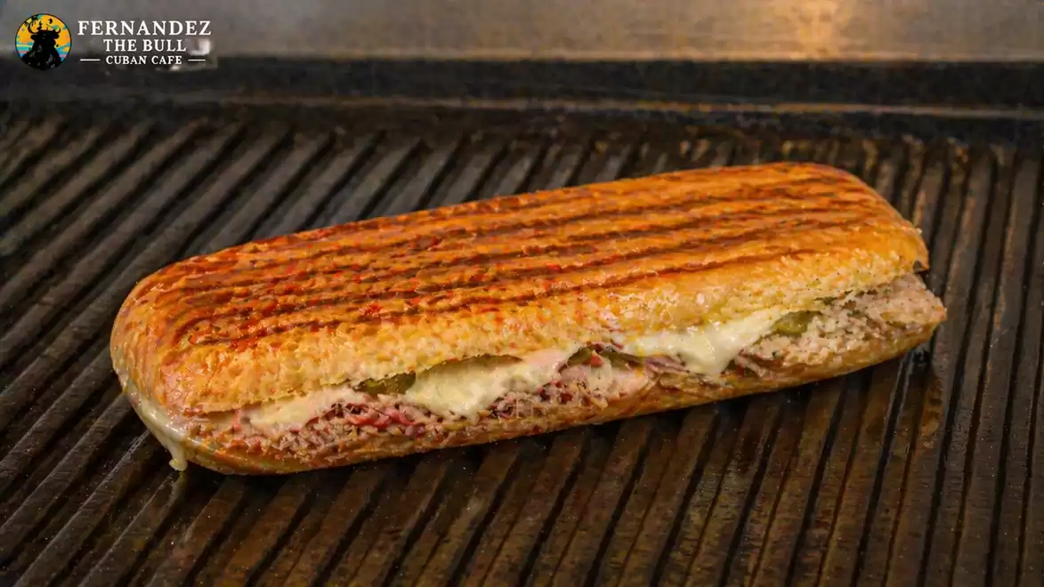 A freshly grilled Cuban sandwich with melted cheese on a grill.