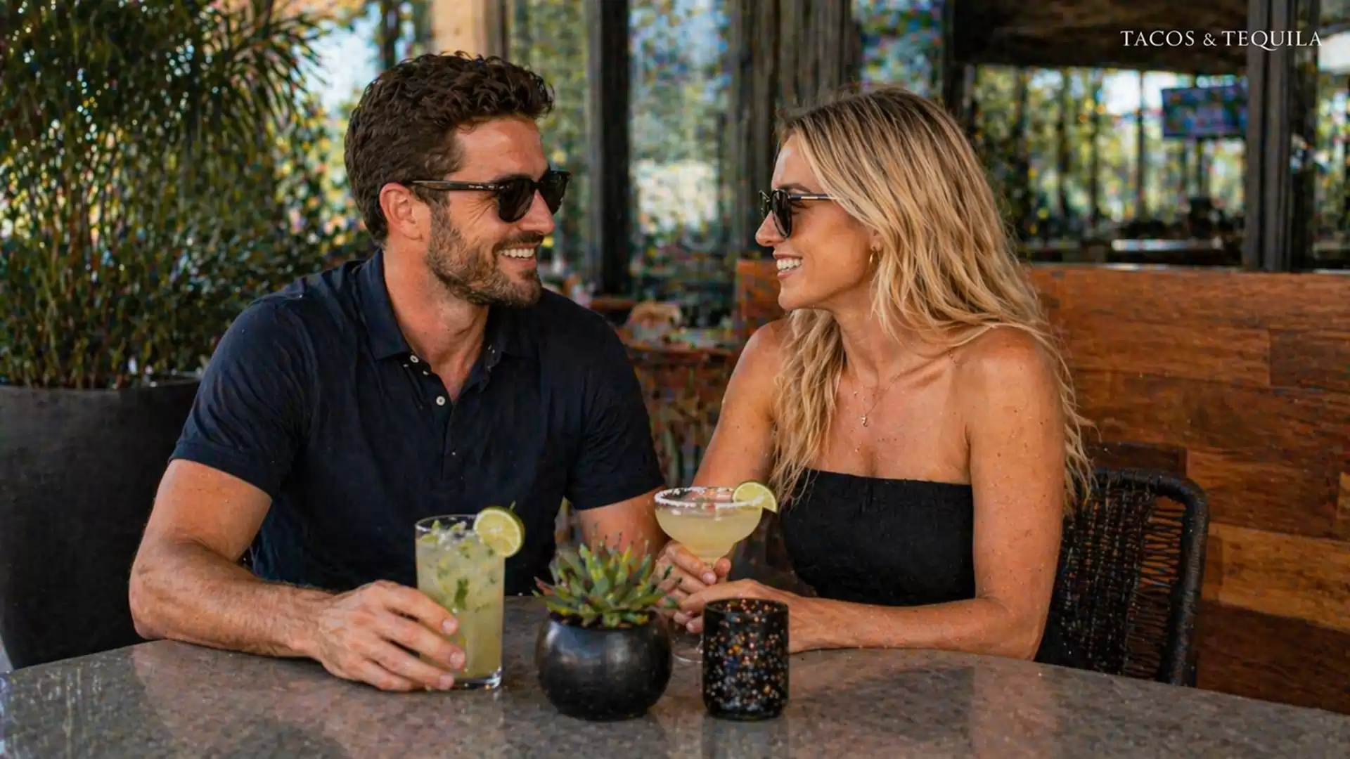 A smiling couple sits at a table enjoying cocktails at Tacos & Tequila.