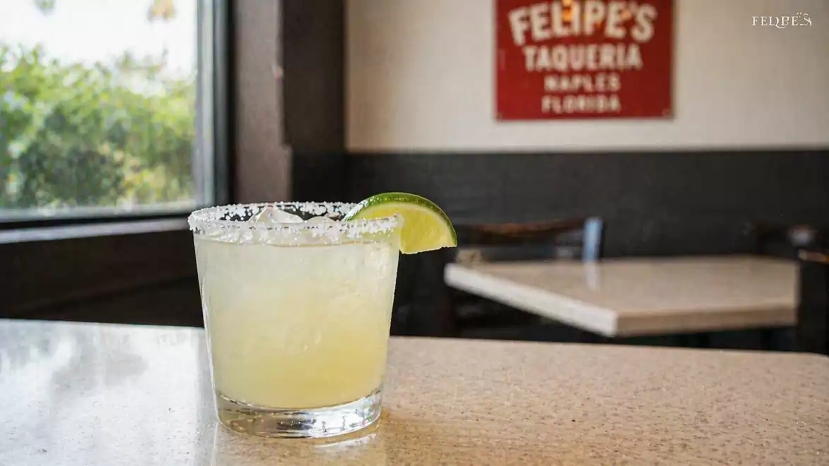 A margarita cocktail with a lime wedge on a counter in a restaurant with a red sign on the wall.