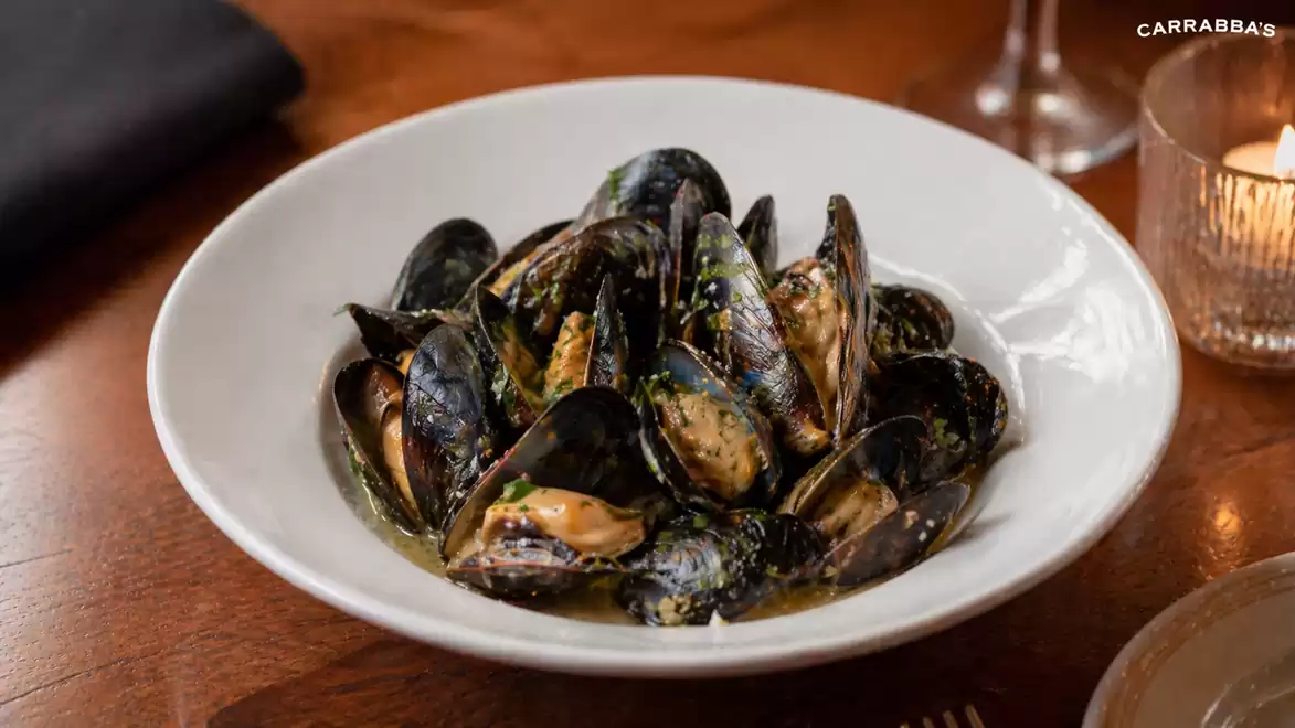 A plate of freshly prepared mussels in aromatic herb sauce on a wooden table.