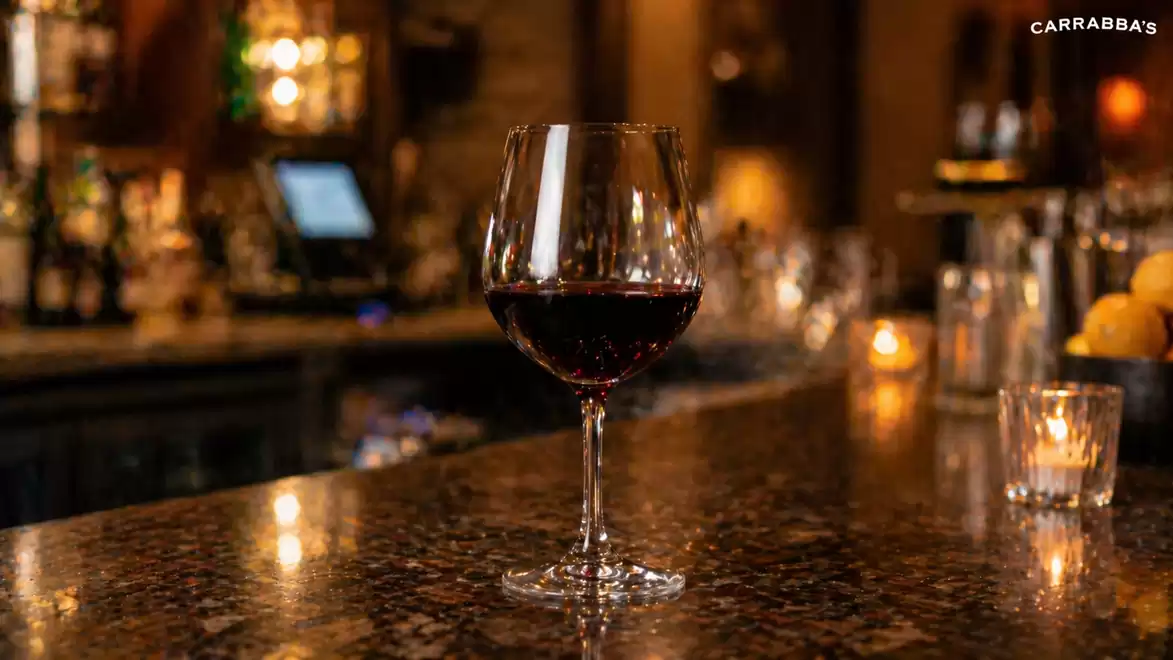 A glass of red wine sits on an elegant bar in a cozy restaurant setting with warm lighting.