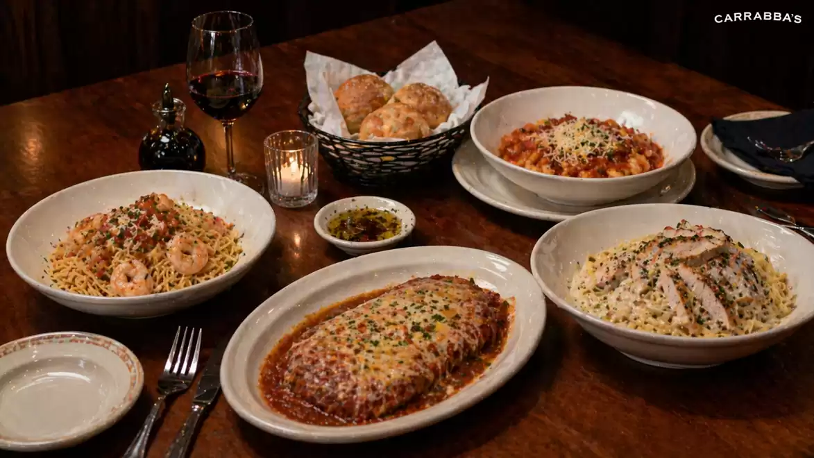 A restaurant table with several Italian dishes including pasta and lasagna, along with a glass of red wine and a basket of bread.