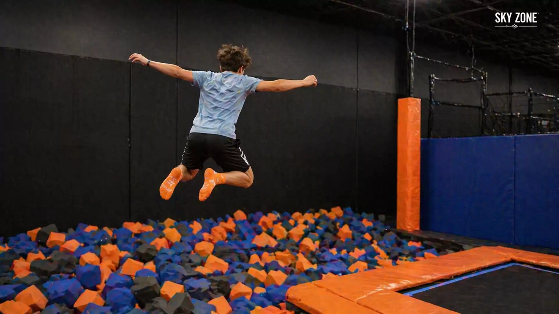 A boy jumps on a trampoline in an indoor play center and leaps into a pool of foam blocks.