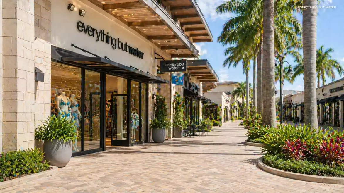 Shopping mall with palm trees, shops, and a sunny promenade.