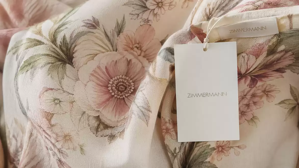 Close-up of a garment with a floral pattern in pink and green. A tag is attached.