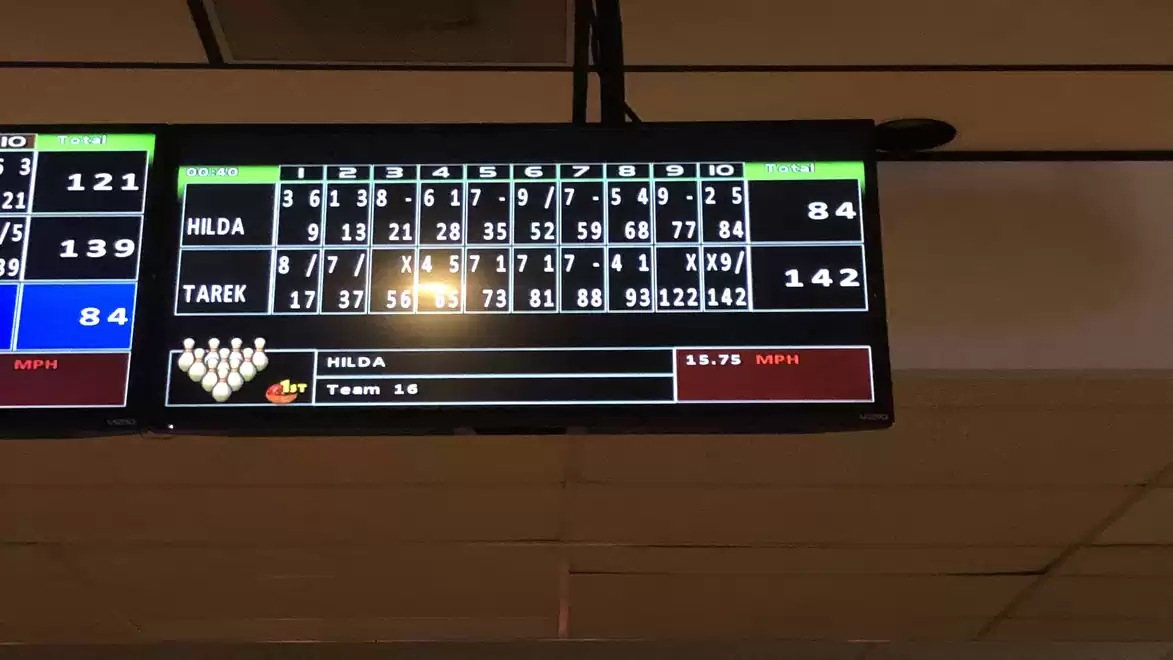 A display screen at a bowling alley shows the scores of a game. The scores for Hilda and Tarek are shown, with Tarek leading.