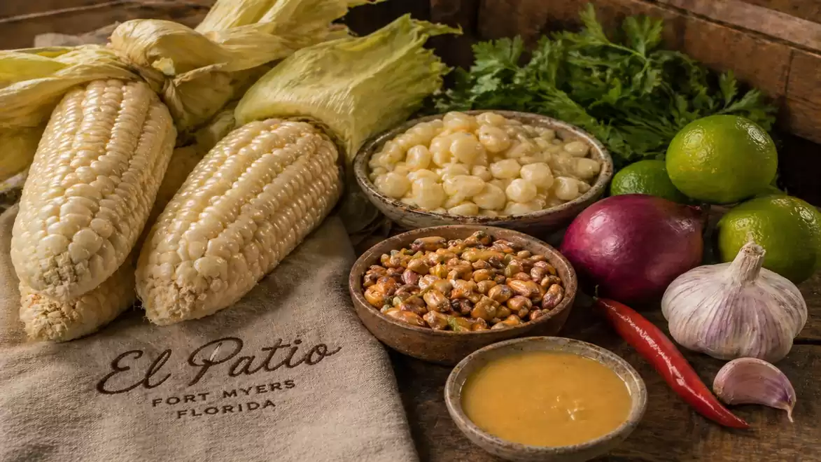 Colorful selection of corn varieties and spices on a wooden table. Various ingredients like corn cobs, limes, onion, garlic, and chili arranged.