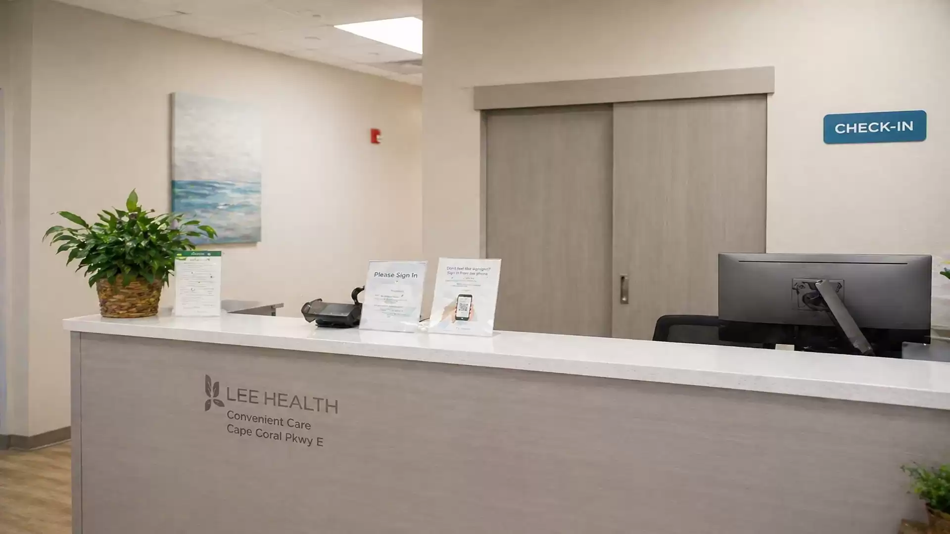 Reception area of a medical facility with check-in sign, computer, and potted plant.