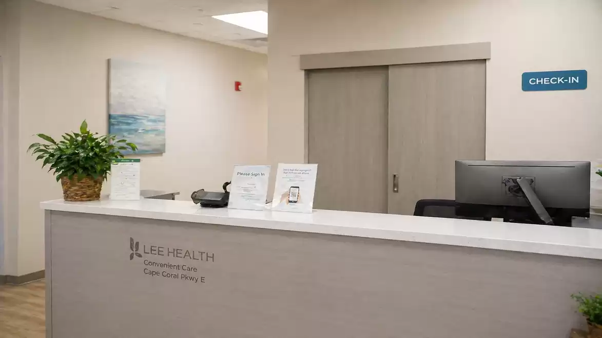 Reception area of a medical facility with check-in sign, computer, and potted plant.