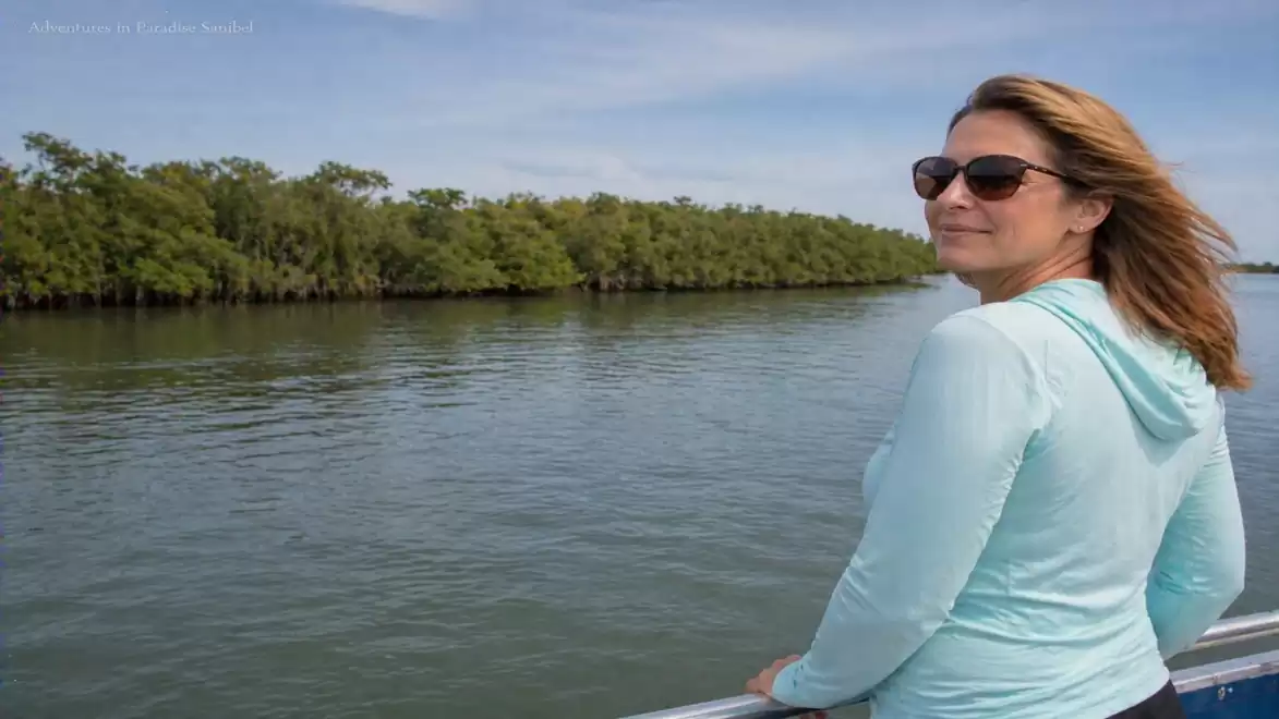 Woman on a boat looking at a wooded river landscape.