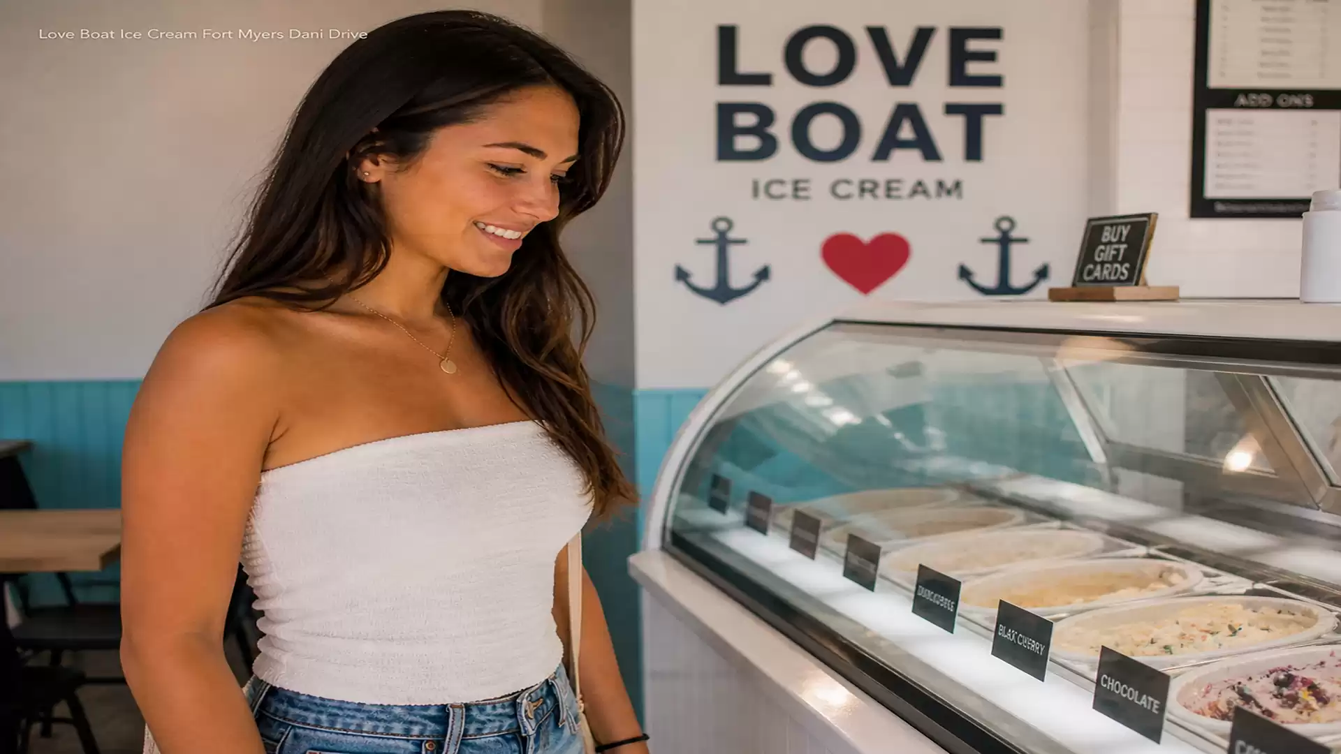 Young woman smiles and looks at an ice cream counter in a parlor with the sign 'Love Boat Ice Cream'.
