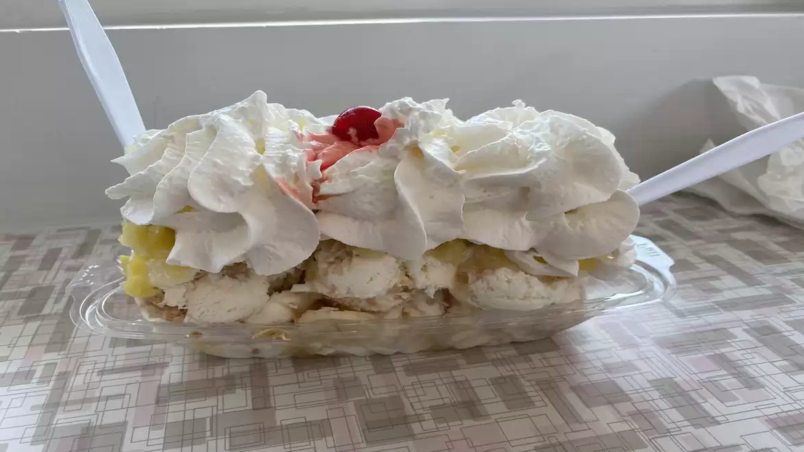 A banana split ice cream sundae with whipped cream, a cherry, and plastic spoons on a table.