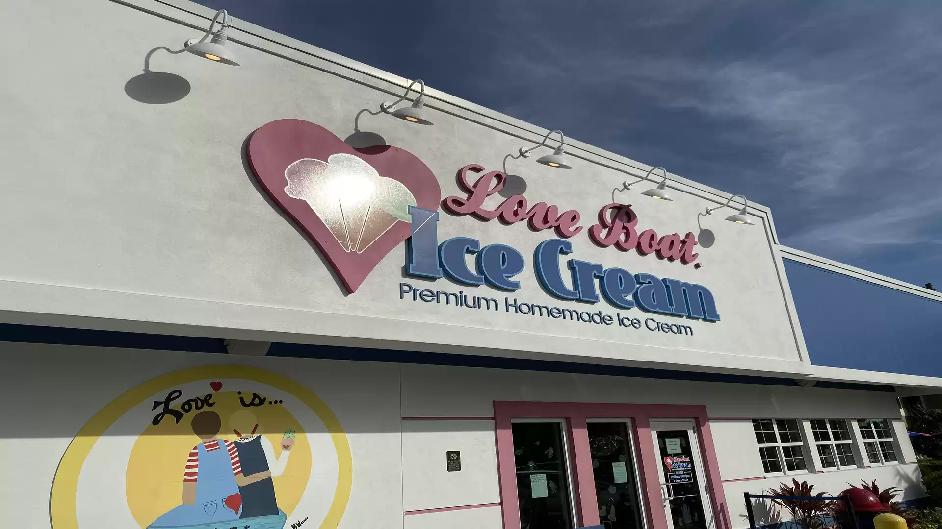 Exterior view of a shop named 'Love Boat Ice Cream', an ice cream parlor with a heart logo and blue lettering under a blue sky.