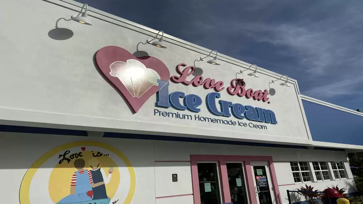 Exterior view of a shop named 'Love Boat Ice Cream', an ice cream parlor with a heart logo and blue lettering under a blue sky.