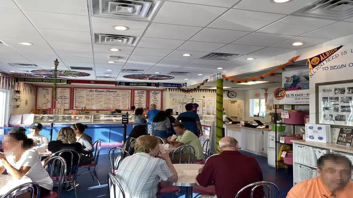 Interior view of an ice cream shop with several guests sitting at tables and staff working behind the ice cream counter.