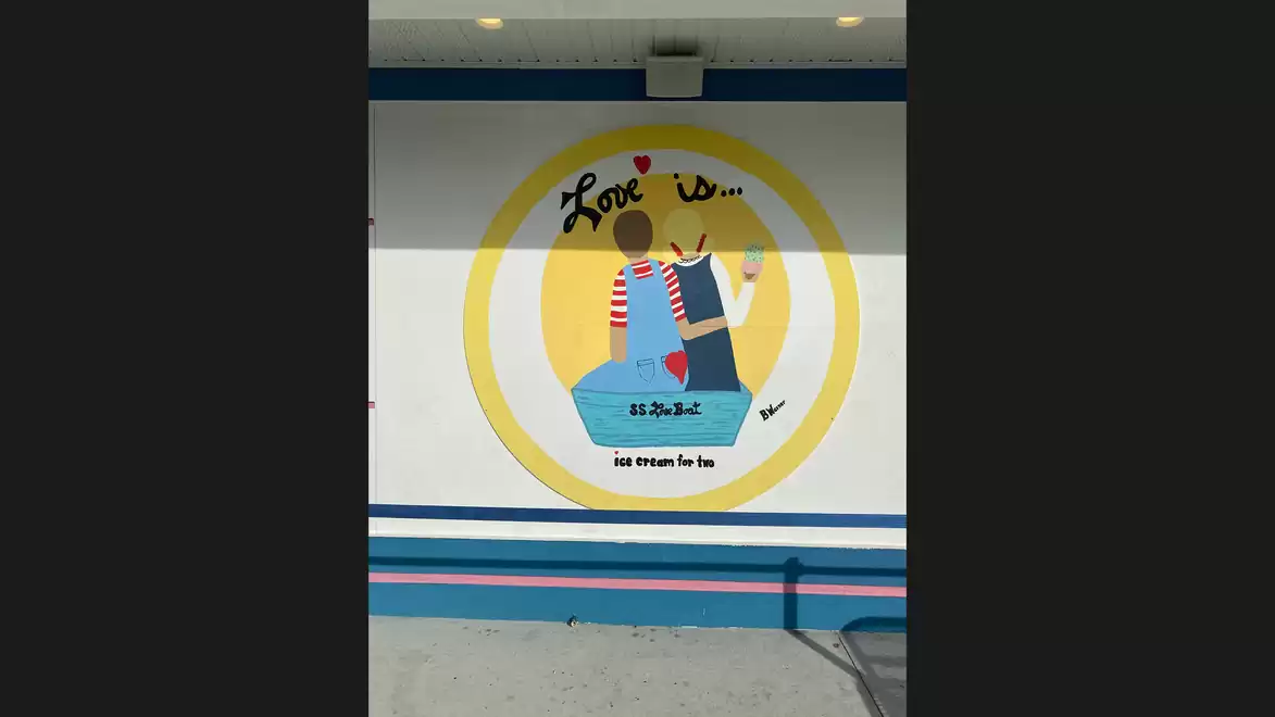 Mural of a couple sitting back-to-back, surrounded by a yellow circle, with the text 'Love is...'.