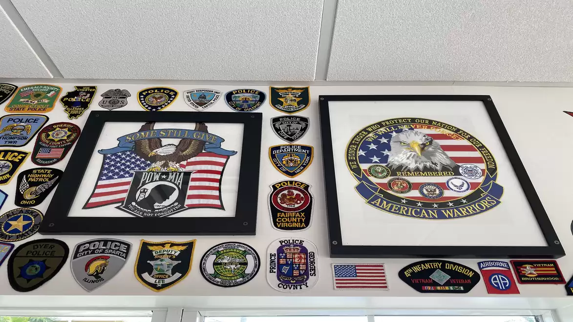 A wall display featuring various police badges and patches, including two framed pictures with American flag motifs.