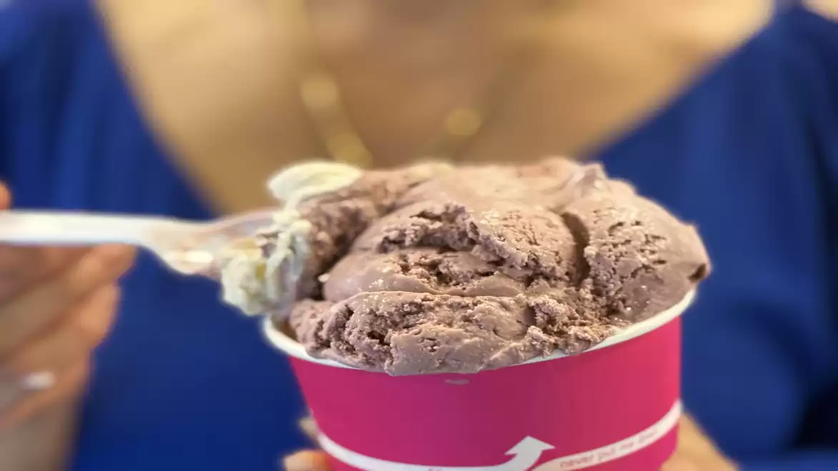 Close-up of a person holding a pink cup with chocolate ice cream, with blue clothing in the background.