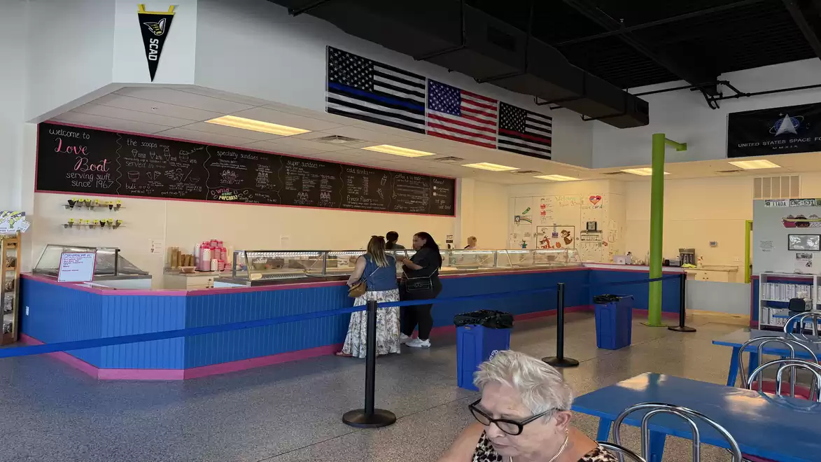 Interior of an ice cream parlor with blue counters and three people ordering ice cream. American flags on the wall.