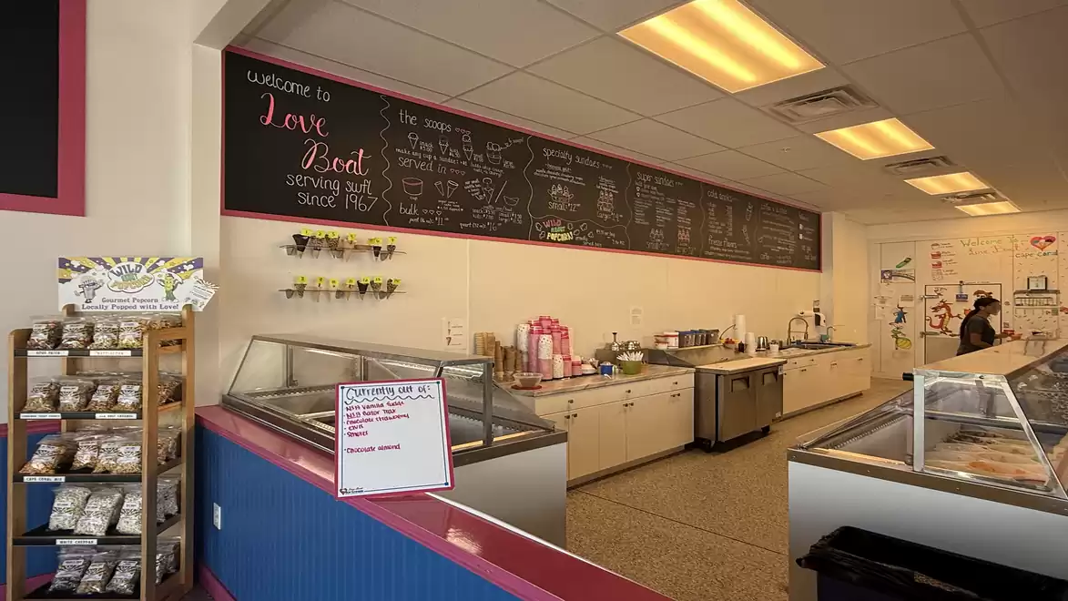 Interior view of an ice cream shop with a selection of products on a shelf and a long counter with ice cream machines.
