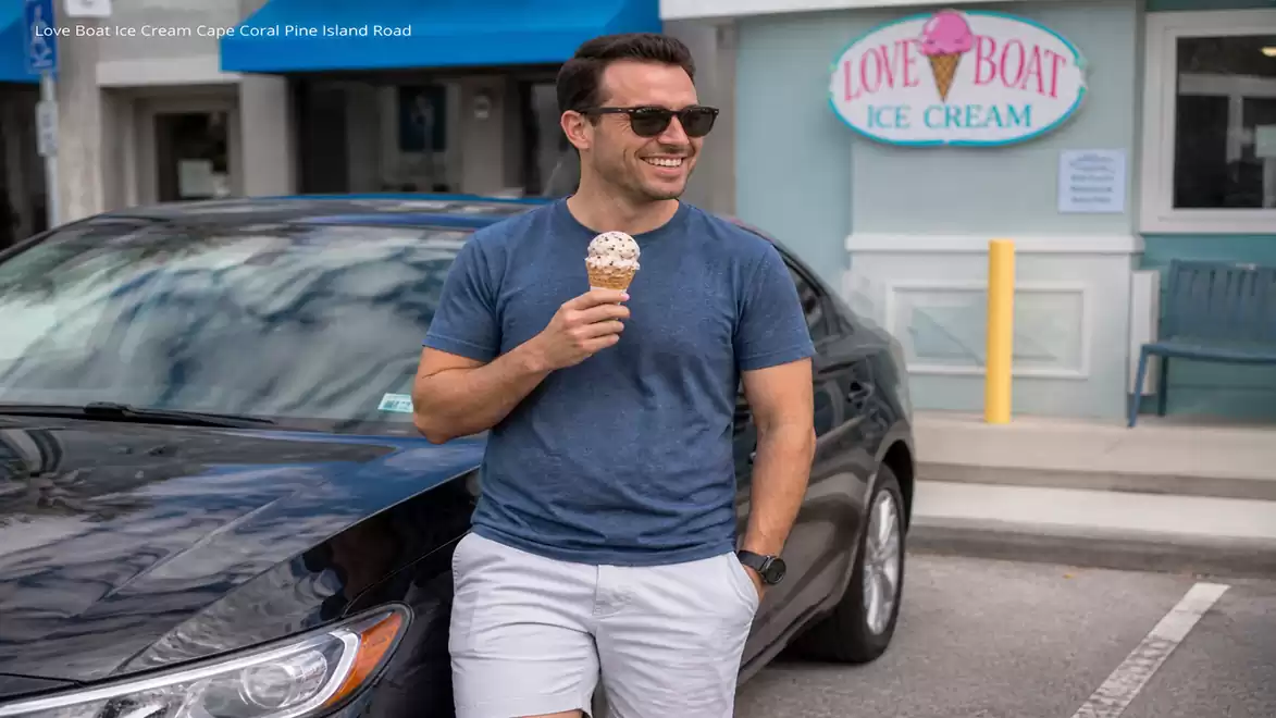 Man with sunglasses holding an ice cream and leaning against a black car in front of an ice cream shop.