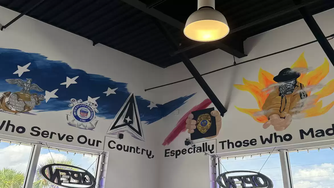 Wall painting in a room honoring various military and rescue services, featuring artistic emblems and the text 'Who Serve Our Country, Especially Those Who Made.'