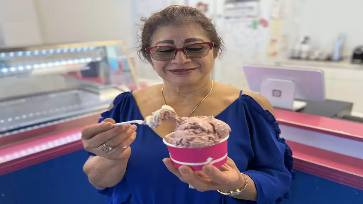 Woman in a blue blouse holding an ice cream cup with pink ice cream in a store.