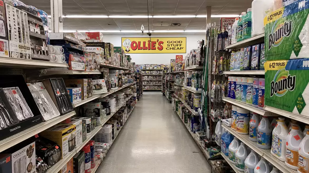 An aisle in a retail store filled with household products like paper towels and cleaning supplies.