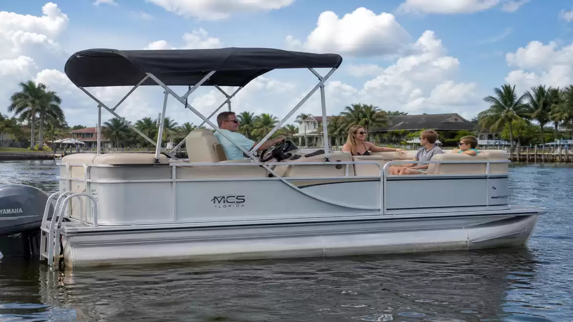 A family sitting on a pontoon boat on a lake with blue sky and clouds in the background.