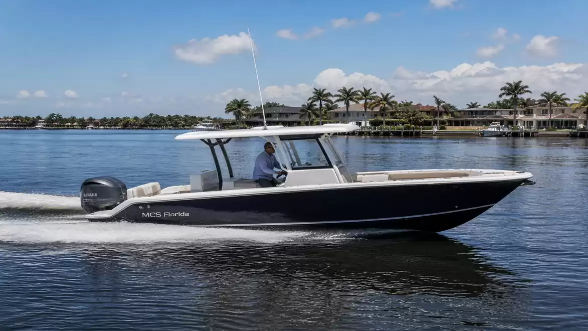 A modern motorboat cruising on calm waters with palm trees on the shore in the background.