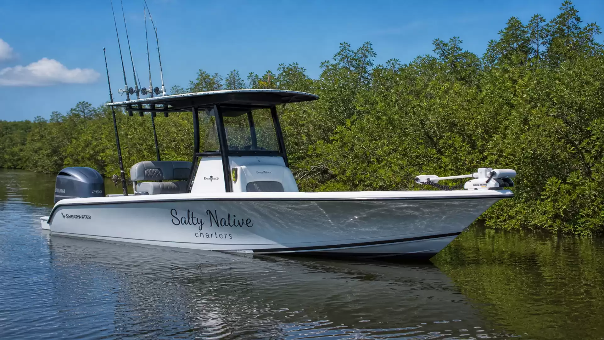 A modern fishing boat floats on calm water with green trees in the background.