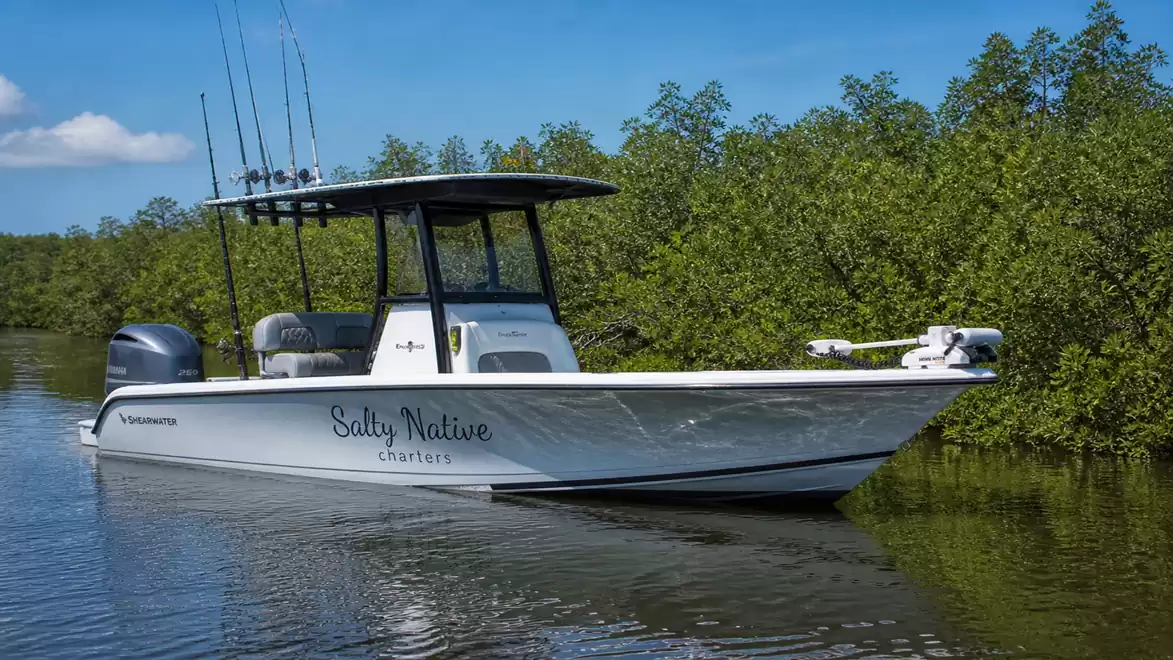 A modern fishing boat floats on calm water with green trees in the background.