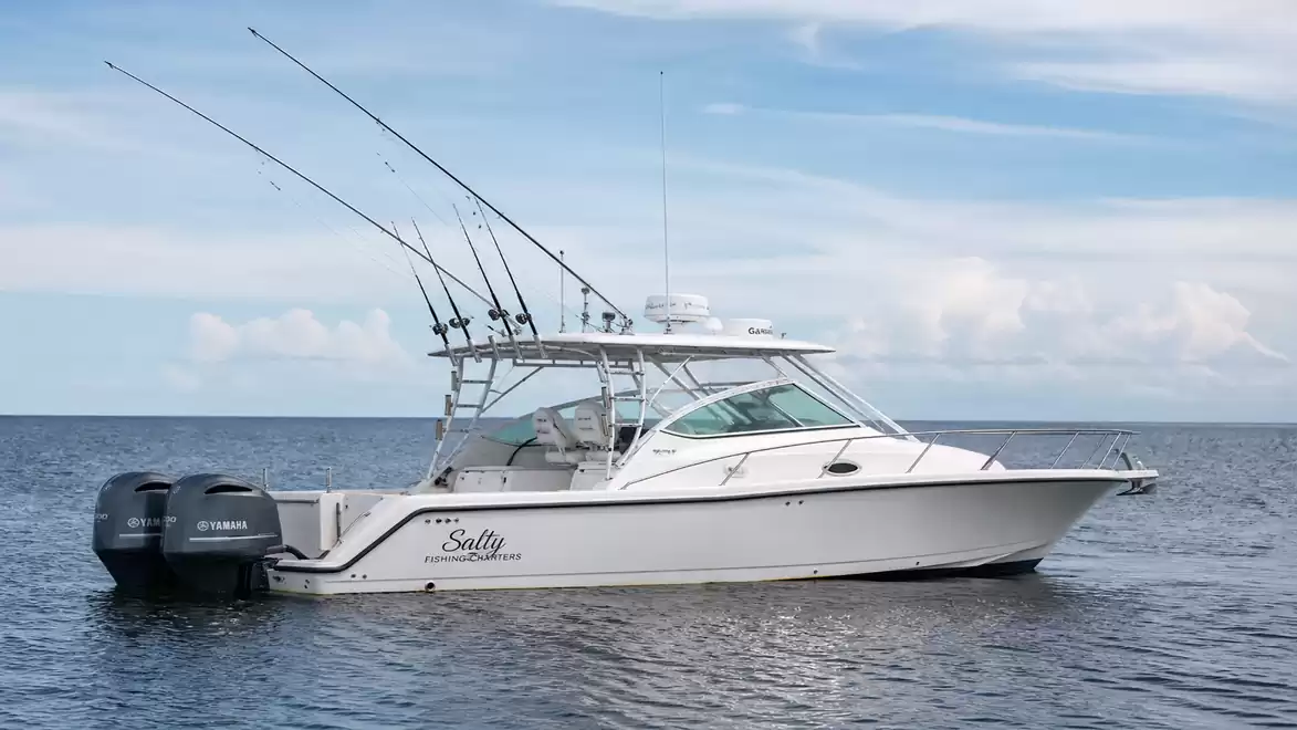 A sporty white boat with multiple fishing rods floating calmly on a blue sea under a clear sky.